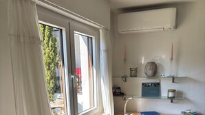Une petite pièce comprenant un bureau en bois, une chaise, un radiateur, une fenêtre avec des rideaux et une plante en pot.