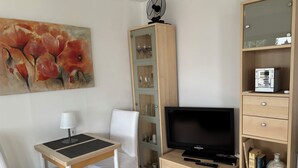 Un salon moderne avec un téléviseur à écran plat, une table à manger avec des chaises, un meuble avec des portes en verre et un tableau accroché au mur.