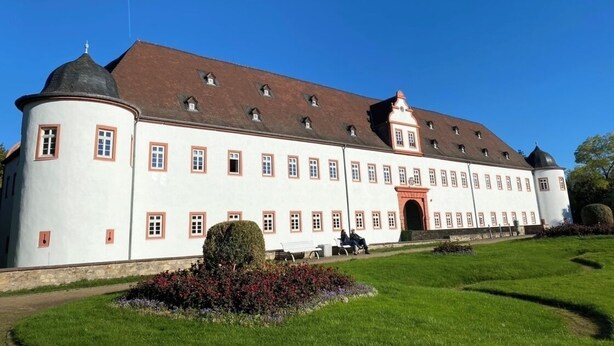 Un grand bâtiment blanc à la façade symétrique, doté de nombreuses fenêtres et d’une entrée centrale.