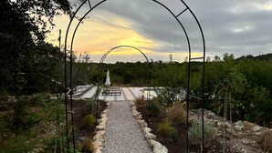 A pathway leading to a seating area with a view of a pool and a sunset. - Designer Luxury Cottage with Saltwater Pool on Private 4 Acres (Johnson City)