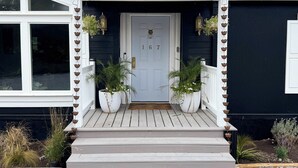 A house with a white front door, a porch with steps, and two potted plants on either side. - Designer Luxury Cottage with Saltwater Pool on Private 4 Acres (Johnson City)