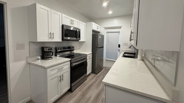 A modern kitchen with white cabinets, stainless steel appliances, and a light-colored countertop. - Location Lake Eola View 1 Bedroom condo (Orlando)