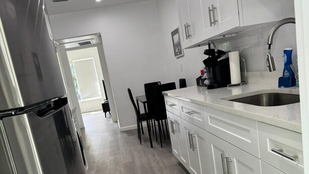 A modern kitchen with white cabinets, a stainless steel refrigerator, and a black countertop.