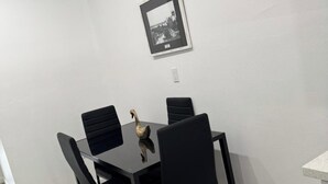 Een eetgedeelte met een zwarte tafel en stoelen, een lijst met afbeelding aan de muur, en een klein plankje.