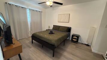 Une chambre à coucher avec un lit, un bureau avec un ordinateur, un ventilateur de plafond et une table de chevet.