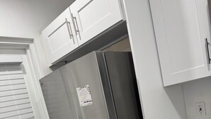 A kitchen with white cabinets, a stainless steel refrigerator, and a window with blinds.