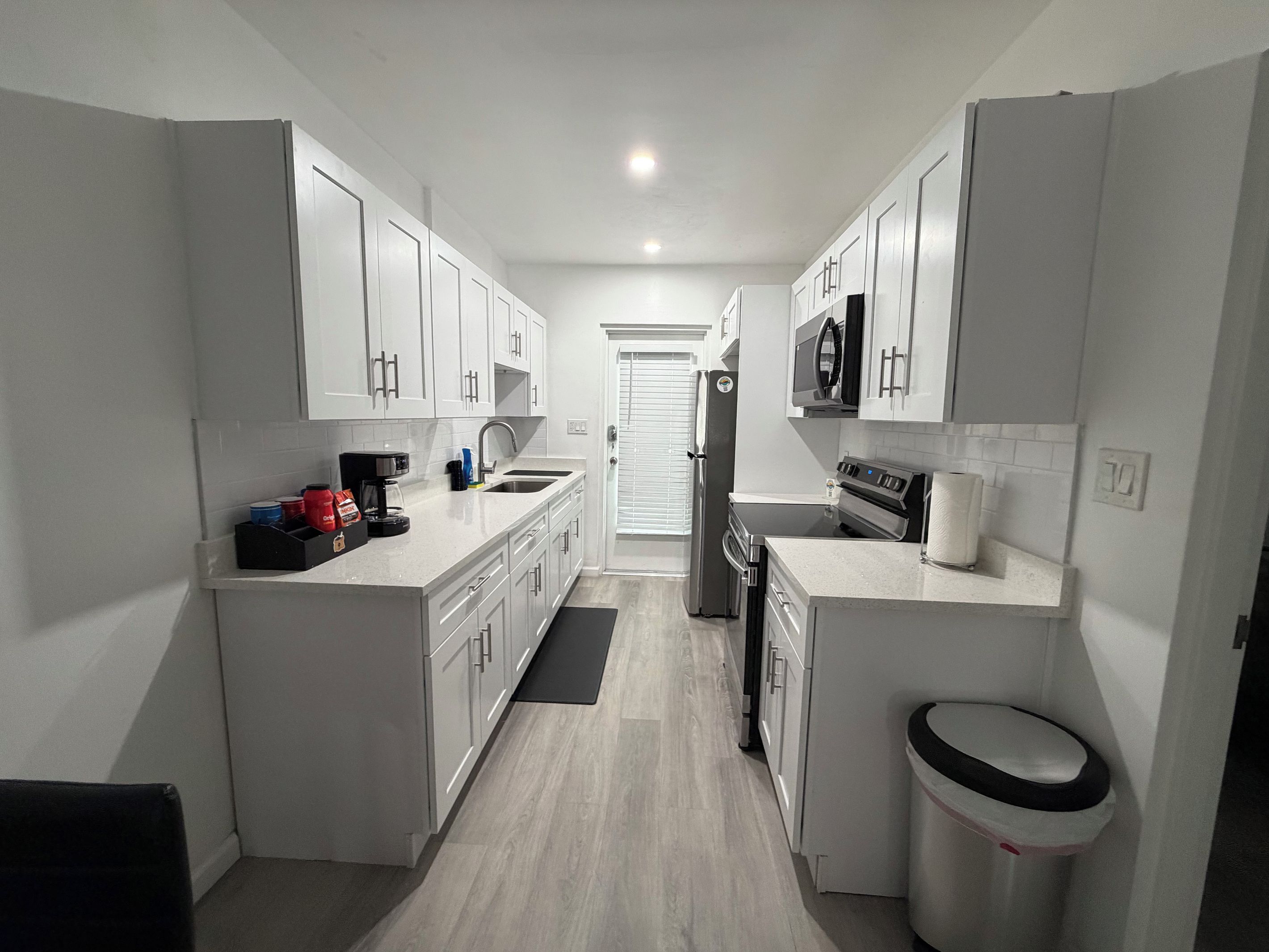 A modern kitchen with white cabinets, a stainless steel refrigerator, a microwave, and a stove.