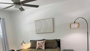 A bedroom with a bed, a ceiling fan, a bedside lamp, a nightstand, and a wall-mounted artwork.
