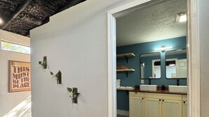 Un baño con pared blanca, un espejo, un lavabo y un armario. Hay tres plantas verdes en la pared.
