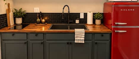 A modern kitchen with dark cabinets, a red refrigerator, a microwave, and a wooden countertop.