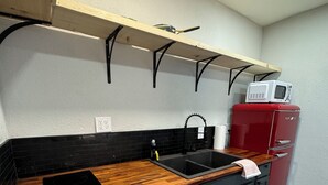 Una cocina compacta con encimera de madera, salpicadero negro y refrigerador rojo.