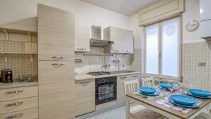 Eine moderne Küche mit hellen Holzschränken, einem eingebauten Backofen und einem Fenster mit Vorhängen.