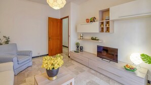 Ein modernes Wohnzimmer mit einer Couch, einem Couchtisch mit Blumen, einem Fernseher und einer Schrankwand mit Regalen.