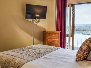 A bedroom with a bed, a wooden dresser, a television on the wall, and a view of the outdoors through a window. - 3 bedroom accommodation in Carnforth (Carnforth)