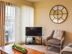 A living room with a TV on a stand, a grey armchair, and a wooden coffee table with a plant. - 3 bedroom accommodation in Carnforth (Carnforth)