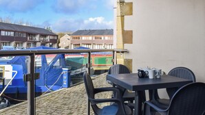 A balcony with a table and chairs, overlooking parked vehicles and buildings. - 3 bedroom accommodation in Carnforth (Carnforth)