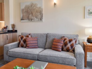 A grey sofa with patterned cushions, a wooden coffee table, and a painting of trees on the wall. - 3 bedroom accommodation in Carnforth (Carnforth)