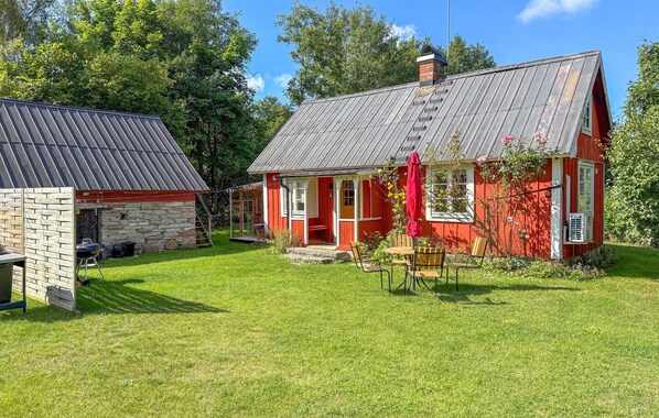 A red house with a porch and a stone building in the background.