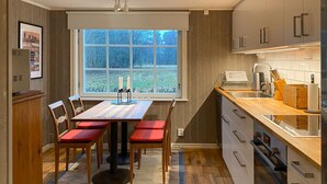 Une cuisine moderne avec un coin repas, dotée d’une grande fenêtre, de meubles en bois et d’un îlot central avec des sièges.