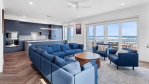 A modern living room with a large sectional sofa, a coffee table, and a view of the ocean through large windows.