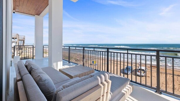 A balcony with a view of the ocean, a wooden deck, and a seating area with cushions.