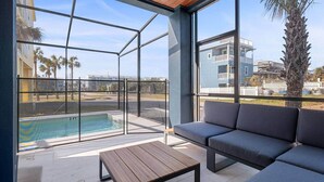 A modern outdoor patio with a pool, a wooden table, and a gray sofa.