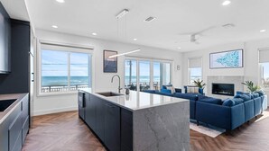 A modern kitchen with a large island, a dining area with a blue sofa, and a view of the ocean.