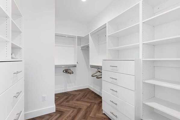 Un vestidor con estanterías blancas, cajones y un suelo de madera con estampado de espiga.