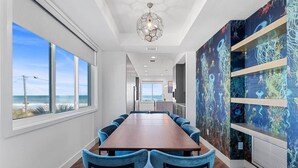 A modern conference room with a long table and blue chairs, large windows with a view of the ocean, and a wall with an ocean-themed mural.