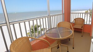 A balcony with wicker chairs and a glass table, overlooking a beach and ocean. - Casa Playa #403 Beach Front - Dolphin Watch (Fort Myers Beach)