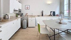 Eine moderne Küche mit weißen Schränken, ein Essbereich mit weißem Tisch und Stühlen sowie ein Fenster, das für natürliches Licht sorgt.