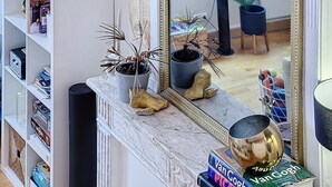 Ein Marmor-Kamin mit Dekoration, ein Bücherregal mit Büchern und ein Spiegel, der den Raum reflektiert.