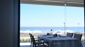 Et spisebord med stole, havudsigt og strandparasoller i baggrunden.