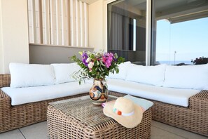 A wicker sofa with white cushions, a wicker coffee table, a vase with flowers, and a straw hat.