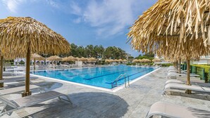 A swimming pool with clear blue water, surrounded by lounge chairs and thatched umbrellas.