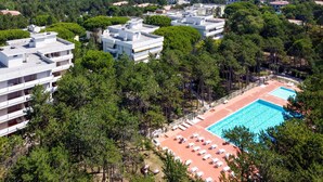 A residential area with modern apartment buildings, a swimming pool with sun loungers, and surrounding greenery.