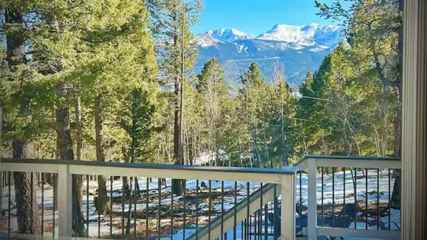 A view from a window with a metal railing, featuring a snowy landscape, trees, and mountains in the distance. - Pikes Peak Views & Hot Tub | Mountain Home (Woodland Park)
