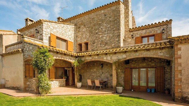 Un edificio de piedra con un patio, que cuenta con un comedor con mesas al aire libre y una gran planta en maceta.