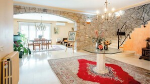 Amplia sala de estar con comedor, candelabro, escalera y alfombra roja.