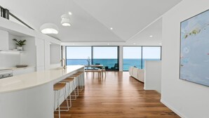 A modern kitchen with a long island, bar stools, and a view of the sea through large windows. - Iluka Lookout | Unforgettable ocean views, new home (Wye River)