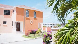Un edificio de dos plantas con techo de tejas rojas, una entrada central con puerta y un pequeño ventanal circular encima de la puerta. Hay macizos de flores coloridos en la parte delantera del edificio.