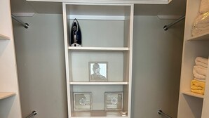 Un armario vestidor con estantes blancos, cajones y una barra para colgar.