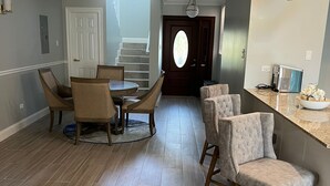 Amplia sala de estar con una mesa y sillas de comedor, zona de cocina con taburetes de bar y una escalera que sube a otro nivel.