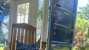 Een houten stoel met een blauw kussen waarop "1902 AVALON SEASONAL 120%" staat, een decoratief figuurtje, een kom noedels, een witte mok en een smartphone op een houten tafel.
