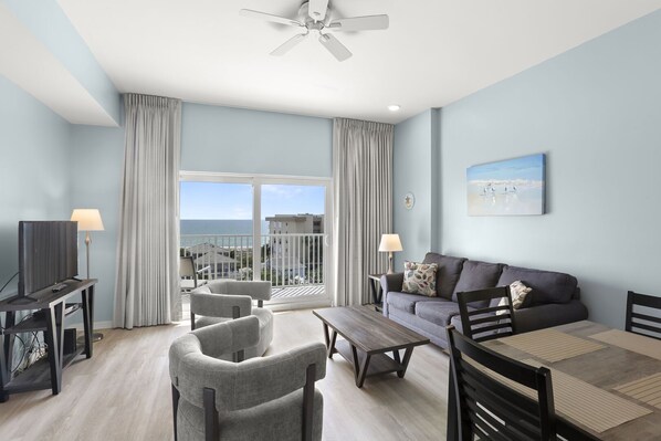 Ein modernes Wohnzimmer mit Balkon, Fernseher, Sofa und Esstisch.