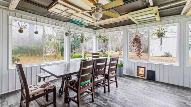 A covered patio with a table and chairs, large windows, and hanging plants.