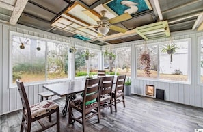 Un patio techado con una mesa y sillas, ventanas amplias y plantas colgantes.