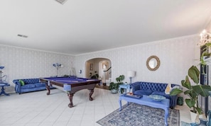 Una sala de estar con mesa de billar, dos sofás azules y una planta en maceta.