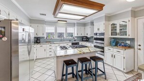 A modern kitchen with white cabinets, a central island, and bar stools.