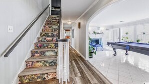 A staircase with floral carpet, a pool table, and a hallway leading to a room with a fireplace.